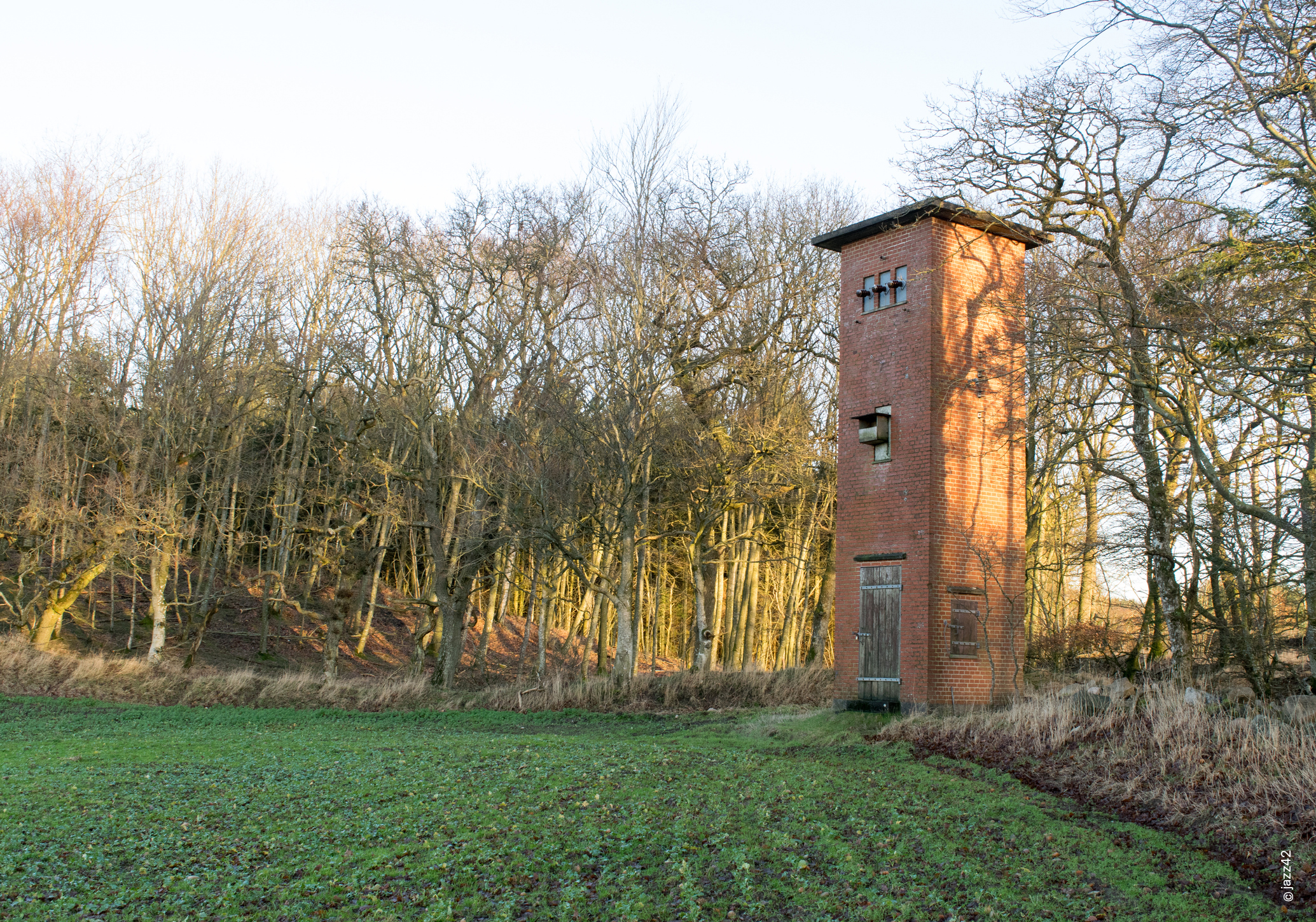 Alter roter Backstein-Trafoturm am Waldrand in winterlicher Landschaft mit kahlen Bäumen.