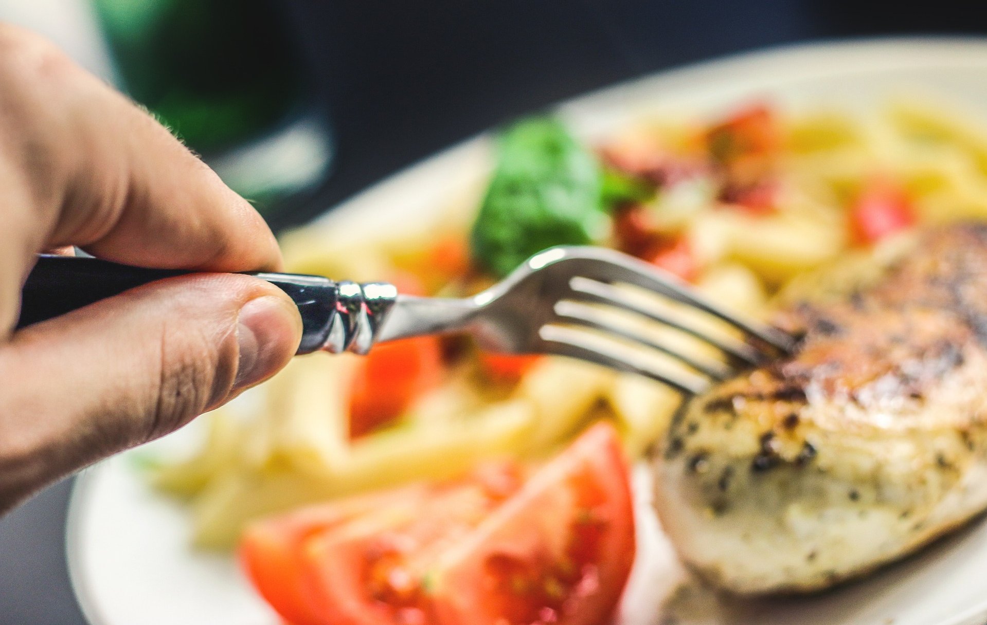 Hand mit einer Gabel nimmt ein Stück Fleisch vom Teller